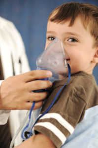 Criança sorrindo fazendo inalação com máscara segurada por médico, possível asma